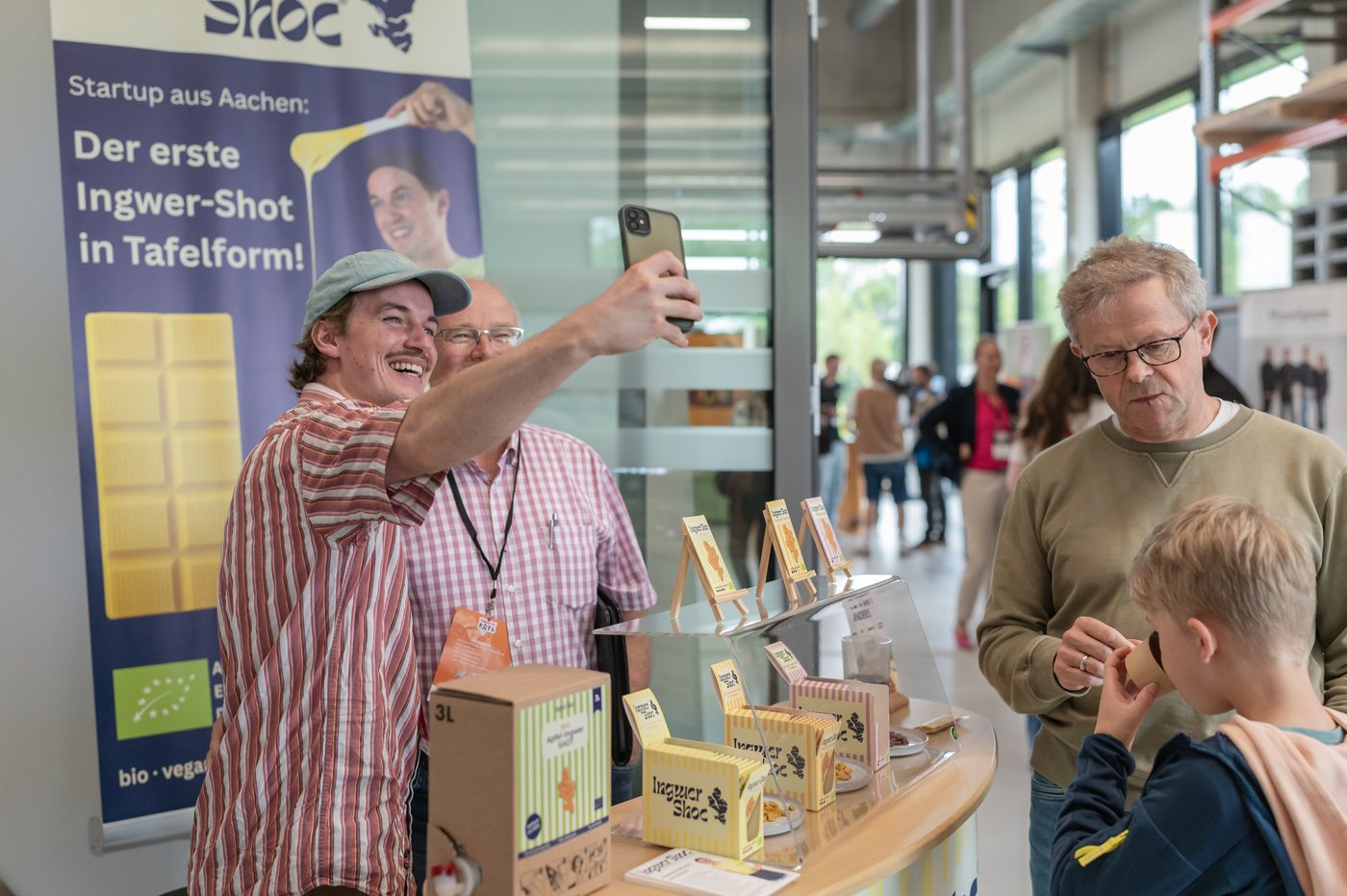 Ein Gründer präsentiert seine Ingwer-Shots am Messestand bei Tomorrow Eats, Besucher probieren die Produkte.