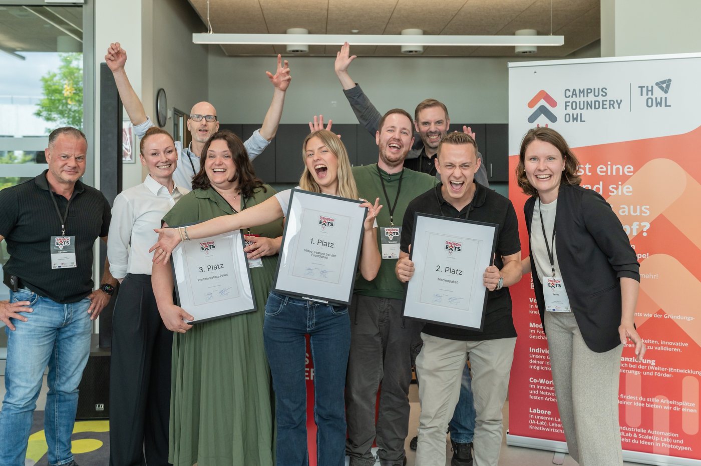 Das Team der Campus Foundery OWL und die Gewinnerinnen und Gewinner des Pitch-Wettbewerbs bei Tomorrow Eats, jubelnd mit den Urkunden für den ersten, zweiten und dritten Platz.